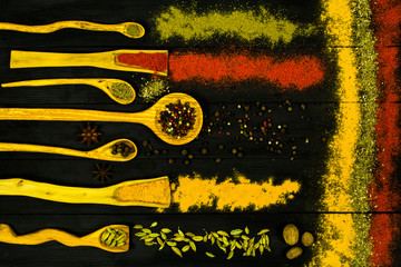 Spoons with spices on a black wooden background.