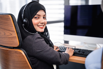 Arabian or Muslim woman works in a call center operator and customer service agent wearing microphone headsets working on computer, talking with customer for assisting with her service mind