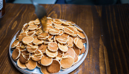 A plate of poffertjes with peanut butter and honey on the wooden background. Dutch mini pancakes ready for breakfast