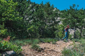 A full body shot of an unrecognizable young Caucasian female hiker with a backpack walking up a path in the French Alps mountains on a sunny summer day