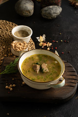 Vegetable soup with beef, potatoes and dill garnished with garlic, chickpeas, black pepper and bay leaf. A bowl of soup and ingredients on a black table.