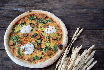 An beautiful vegan pizza with a nice old wooden table with wheat next to it, ideal for designing text around 