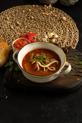 Vegetable soup with noodles, pork, adjika and red pepper. A plate of soup, bread, a tortilla and ingredients on a black table.