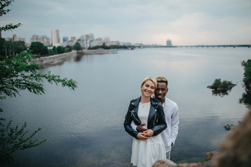 Interracial couple stands against background of river and city.