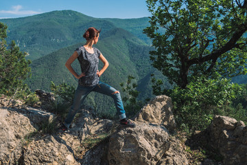Naklejka na ściany i meble A full body shot of an unrecognizable young Caucasian female hiker standing on a rock in the French Alps mountains on a sunny summer day