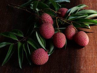 Red lychee fruits and green leaves on a wooden table background, dark tones. Has a pleasant aroma and a thirst-quencher, high vitamin C.