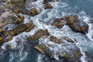 Sea water runs a wave on coastal stones and breaks against them.