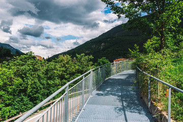 A picturesque view of a metal bridge on a cliff in an old French town in the valley of Var in the Alps mountains on a cloudy day (Puget-Theniers, Alpes-Maritimes, France)
