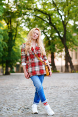 Hipster girl with long blonde hair wearing trendy plaid jacket posing at street. Fashion, lifestyle and people.