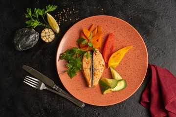 Steamed salmon fillet with fresh vegetables, pepper, zucchini, lemon and carrots with parsley. Hot seafood dish on a black table. Top view.