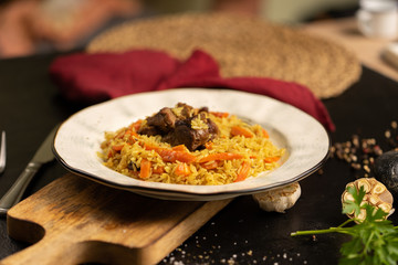 Pilaf with lamb and carrots. Traditional hot oriental dish of lamb and vegetables rice decorated with parsley and garlic on a black table.