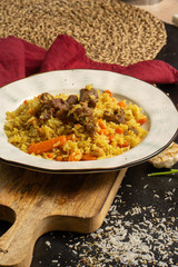 Pilaf with beef and carrots. Traditional hot Georgian rice dish of chicken meat and vegetables decorated with parsley and garlic on a black table.