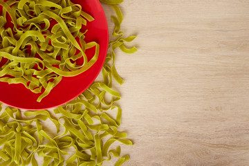 Raw green pasta with spinach on a red plate, top view, copy space