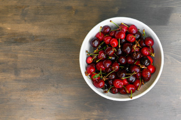 Juicy, ripe, beautiful sweet cherry on a white plate on a wooden background.