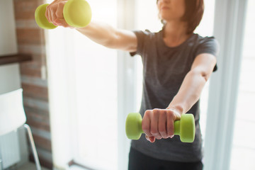 Adult fit slim woman has workout at home. Senior female person exercise using green dumbbells. Take care of health. Well built woman in kitchen. Cut view.