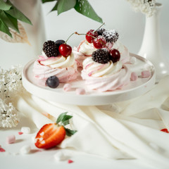 Meringue fruit cake garnished with cream and berries of cherries, blackberries and strawberries, among lilac flowers and green leaves. Food photography. Advertising and commercial close up design.
