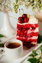 Slised red berry cake decorated with cherry berries and white cream, among lilac flowers and green leaves. Food photography. Advertising and commercial design.