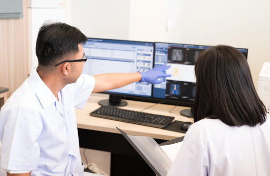 Asian radiologists shows the patient CT scan image at display  and discussion treatment patient information to doctor in x-ray room.High technology for planing medical treatment equipment concept.