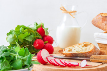 Italian twisted rosemary focaccia bread, ricotta cheese, fresh vegetable and herbs from a garden, radish, arugula, corn salad, sugar pea and milk, wooden mortar with red pepper. White wooden table. 