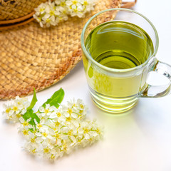 Herbal tea in a glass mug, a straw hat decorated with the color of bird cherry. flat lay