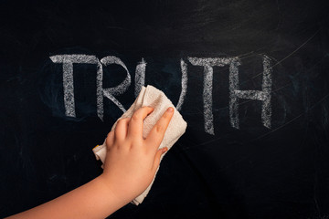 Social issue metaphor - Hand wiping off chalk word truth on chalkboard using rug