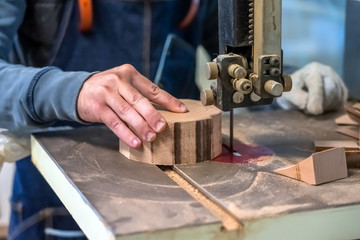 Carpenter is cutting the wooden piece by equipment on stand. The man's hand is making a round detail from the log. Joiner is using Electric fret saw to make a bowl at the workshop.