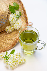 Herbal tea in a glass mug, a straw hat decorated with the color of bird cherry. flat lay