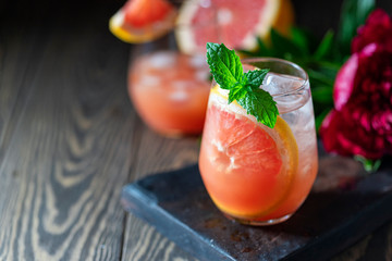A glass of freshly squeezed grapefruit juice and mint on a dark wooden table. Refreshing summer cocktail.