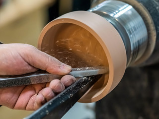 Carpenter man is shaving the wooden bowl. Spinning wood wheel. Carving inside forming a round detail. Joiner is using metal tool to make the handmade pot at workshop. Hand is polishing surface. - obrazy, fototapety, plakaty