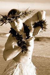 Sepia vintage styled photo of a male hula dancer performing on the sand next to the ocean. 