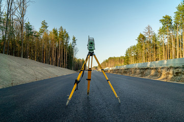 Surveyors equipment (theodolite or total positioning station) on the construction site of the road or building with construction machinery background