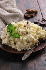 Fermented milk product. Cottage cheese  with chocolate and cookies in a clay plate on an old wooden background. Curd mass, fresh mint, spoon. Rustic. Background image, copy space
