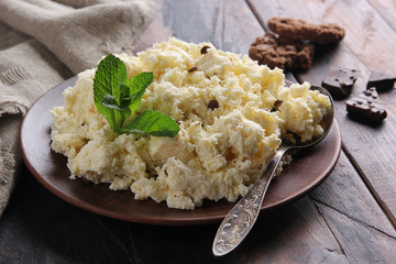 Fermented milk product. Cottage cheese  with chocolate and cookies in a clay plate on an old wooden background. Curd mass, fresh mint, spoon. Rustic. Background image, copy space