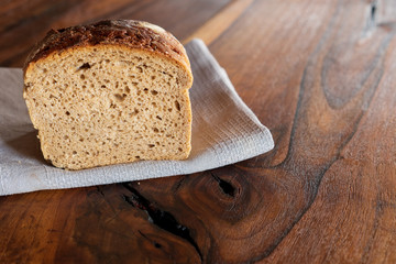 Sourdough bran whole grain bread loaf with walnuts on checkered cotton towel on rustic wood kitchen table. Baking local food specialties concept