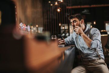 Man drinking beer, smoking cigarette and using mobile phone at pub