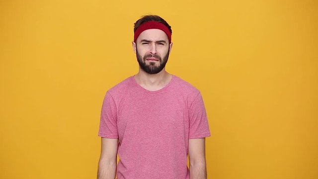 Young bearded fun fitness sporty guy 20s sportsman in headband pink t-shirt isolated on yellow background studio. Workout sport motivation lifestyle concept. Look at camera got ball in head upset cry