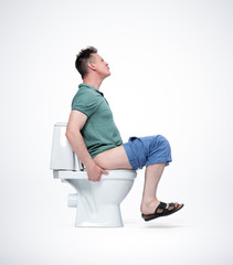 Man in shorts and T-shirt is very tense sitting on the toilet. The concept of situation