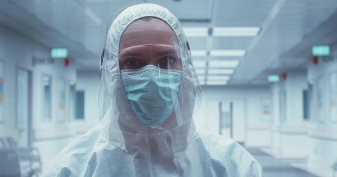 Portrait of Caucasian female doctor posing in a protective suit and face shield in an empty hospitall hallway