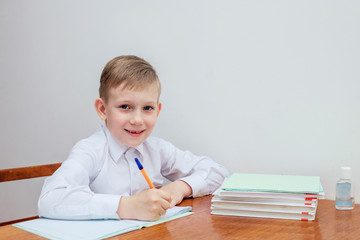 the boy is sitting at the table, holding a pen, next to notebooks and textbooks