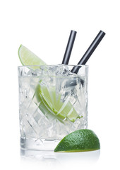 Gimlet cocktail in crystal glass with ice cubes and straw and lime slices on white.