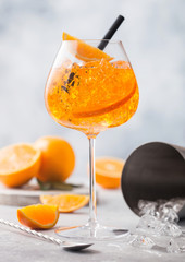 Glass of aperol spritz summer cocktail with oranges bar spoon and cocktail shaker on light background. Ice cubes and black straw.