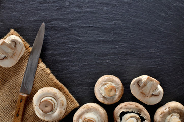 Edible half pieced mushrooms - champignons and rustic knife on vintage slate slab. Copyspace. View from above.