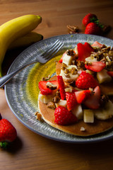 Indulgent banana strawberry and peacan nuts pancakes on a rustic wooden background close up - with whole bananas bunch and whole nuts and strawberries, hot and delicious homecooked brunch