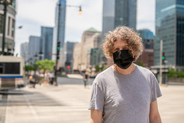 A man wears a black cloth mask while out for a walk downtown in a big city.