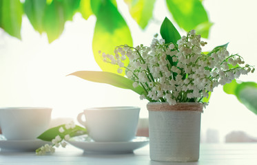 a bouquet of lilies of the valley and a cup of tea on the table close-up. morning tea and a bouquet of lilies of the valley.