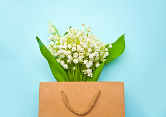 Lily of the valley flowers in a paper bag on blue background. Flat lay, top view, copy space.