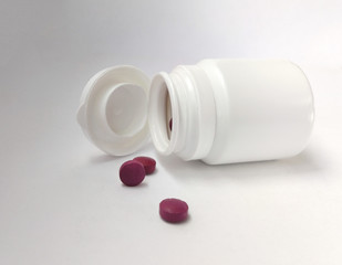 White bottle with purple pills on white background.