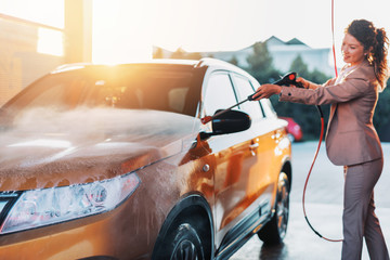 Businesswoman washing car at car wash station using high pressure water machine.