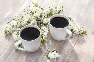 Two beautiful porcelain coffee cups with white cherry flowers on wooden table in spring garden in setting sun light. Top view.