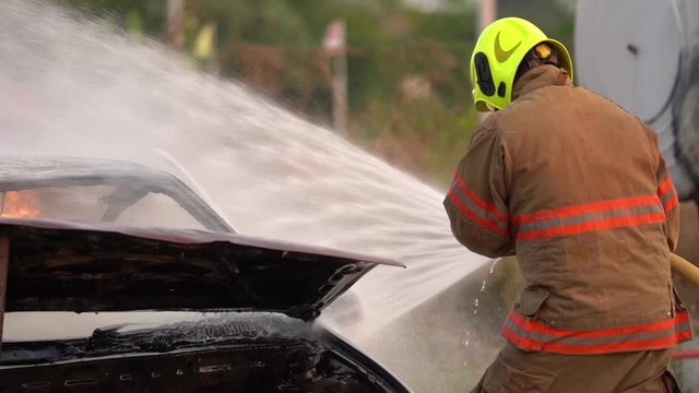 Slow motion/firefighters extinguishing the car caught on fire in a car accident